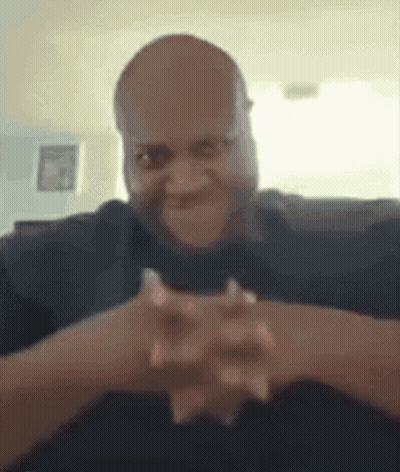 A Man Is Sitting On A Couch With His Hands Folded In Front Of His Face . GIF