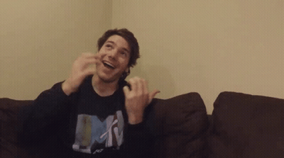 A Man Is Sitting On A Couch With His Hands In The Air And Wearing A Shirt That Says Mtv . GIF