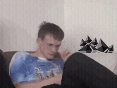 A Man Is Sitting On A Couch With His Legs Crossed And Looking At His Phone . GIF