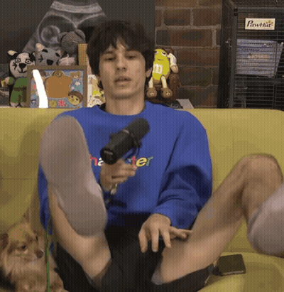 A Man Is Sitting On A Couch With His Legs Crossed Wearing A Blue Shirt That Says Master GIF