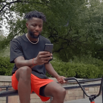 A Man Is Sitting On A Railing Looking At His Phone GIF