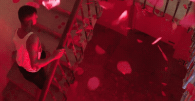 A Man Is Sitting On A Set Of Stairs With Petals Falling From The Ceiling . GIF