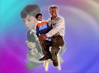 A Man Is Sitting On A Stool Holding A Puppet In His Lap GIF