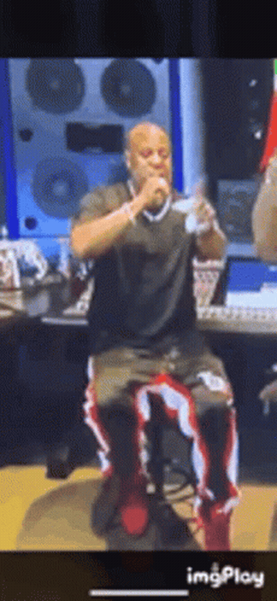 A Man Is Sitting On A Stool Singing Into A Microphone In A Recording Studio . GIF