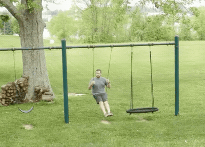 A Man Is Sitting On A Swing In A Park . GIF