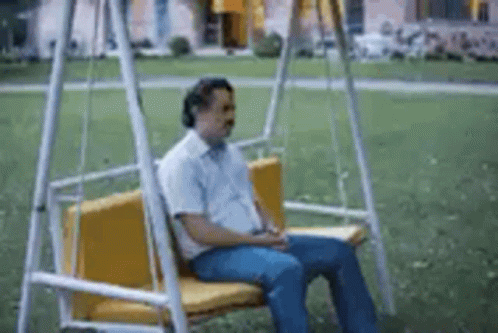 A Man Is Sitting On A Swing In A Park With His Head Down . GIF