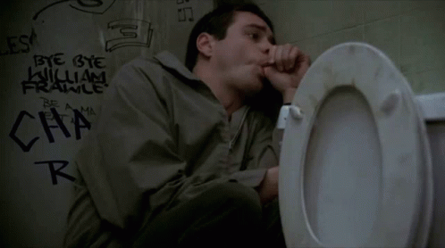 A Man Is Sitting On A Toilet In A Bathroom With Graffiti On The Wall Behind Him . GIF