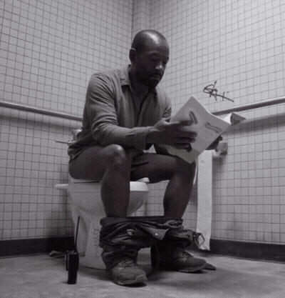 a man is sitting on a toilet reading a book titled " a man 's manual "