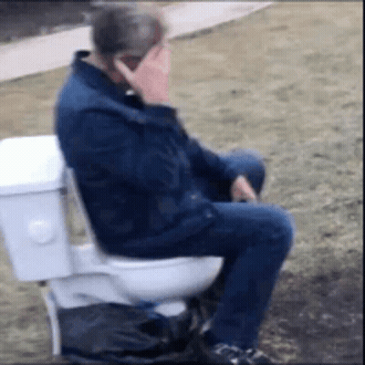 A Man Is Sitting On A Toilet Talking On His Cell Phone . GIF