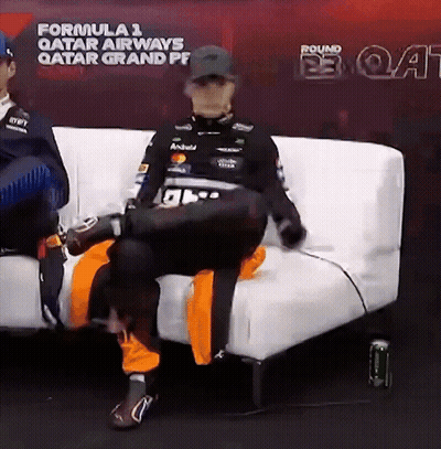 A Man Is Sitting On A White Couch In Front Of A Sign That Says Formula 1 Qatar Airways GIF