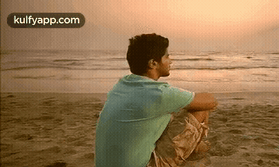A Man Is Sitting On The Beach And Looking At The Ocean . GIF