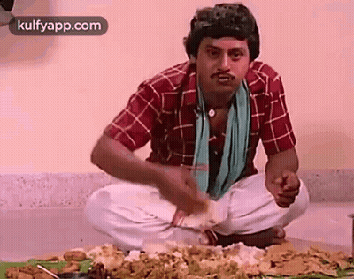 A Man Is Sitting On The Floor Eating Food From A Table . GIF