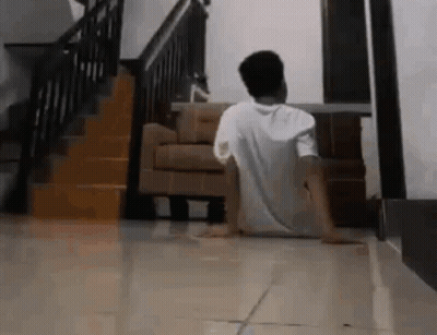 A Man Is Sitting On The Floor In A Living Room In Front Of A Staircase . GIF