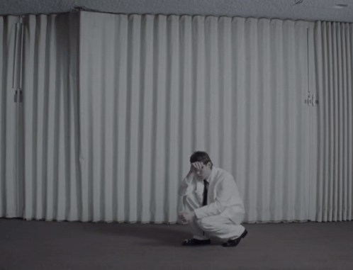 A Man Is Sitting On The Floor With His Head Down GIF