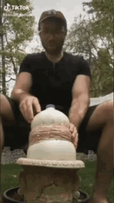 A Man Is Sitting On The Ground With A Milk Bottle On Top Of Him . GIF