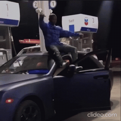 A Man Is Sitting On The Hood Of A Car At A Gas Station GIF