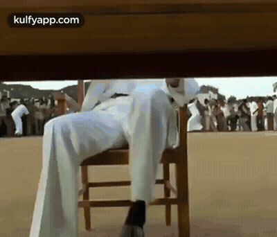 A Man Is Sitting Under A Table With His Legs Crossed . GIF
