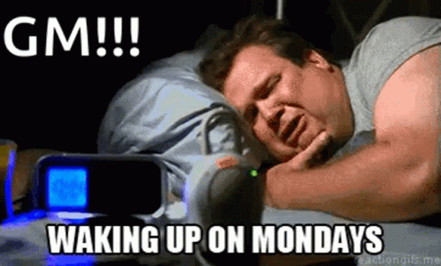 A Man Is Sleeping In A Bed Next To An Alarm Clock And A Gm !!! Waking Up On Mondays . GIF