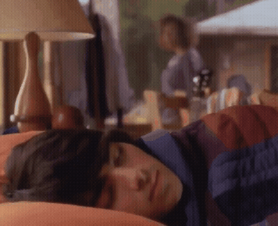 A Man Is Sleeping In A Bed With A Lamp And A Woman Standing In The Background . GIF