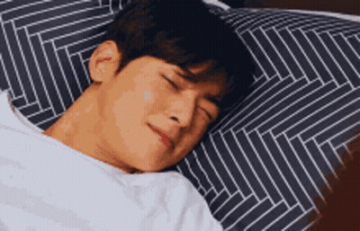 A Man Is Sleeping In A Bed With A Striped Pillow And A White Blanket . GIF