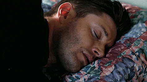 A Man Is Sleeping In A Bed With His Eyes Closed And A Floral Blanket . GIF