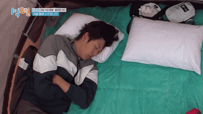A Man Is Sleeping On A Bed With A Bag That Says ' Reebok ' On It GIF