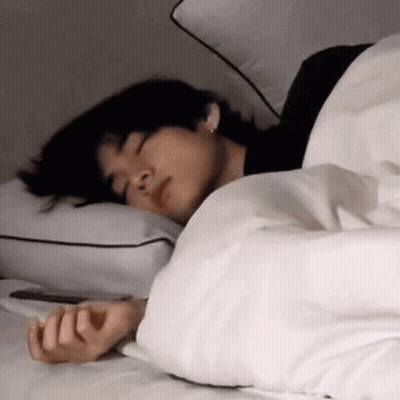 A Man Is Sleeping On A Bed With A White Blanket And Pillows . GIF