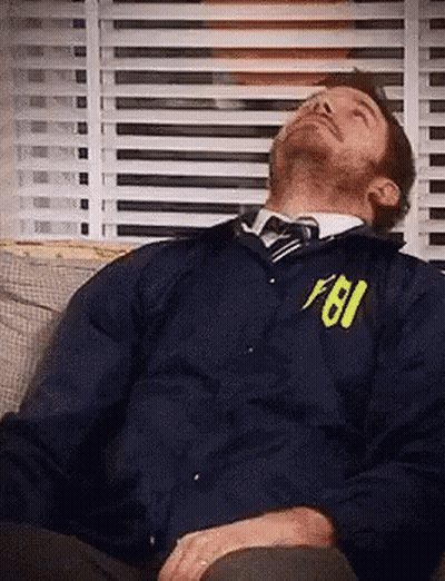 A Man Is Sleeping On A Couch Wearing A Fbi Jacket And Tie . GIF