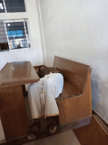 A Man Is Sleeping On A Wooden Bench In A Room GIF