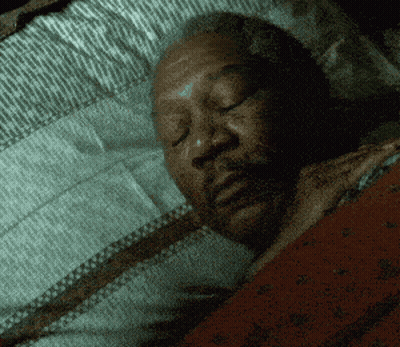 A Man Is Sleeping With His Eyes Closed In A Dark Room GIF
