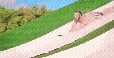 A Man Is Sliding Down A Water Slide In A Park . GIF