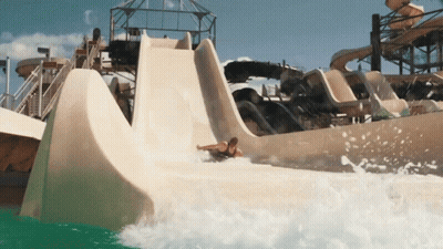 A Man Is Sliding Down A Water Slide In A Water Park GIF