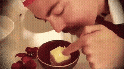 A Man Is Smelling A Piece Of Butter In A Bowl . GIF