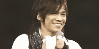 A Man Is Smiling And Holding A Microphone In His Hand . GIF
