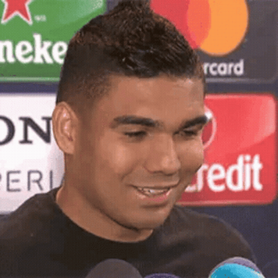 A Man Is Smiling And Talking Into A Microphone While Standing In Front Of A Heineken Sign . GIF