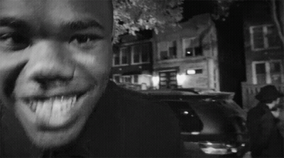 A Man Is Smiling In A Black And White Photo With A Car In The Background GIF