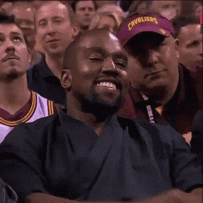 A Man Is Smiling In A Crowd Of People While Wearing A Purple Hat . GIF