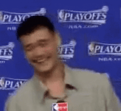 A Man Is Smiling In Front Of A Blue Wall That Says Playoffs . GIF
