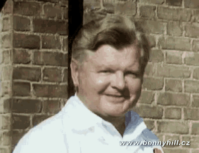 A Man Is Smiling In Front Of A Brick Wall With The Website Www.bennyhill.cz Visible GIF