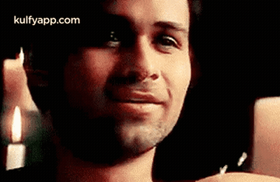 A Man Is Smiling In Front Of A Candle And Looking At The Camera . GIF