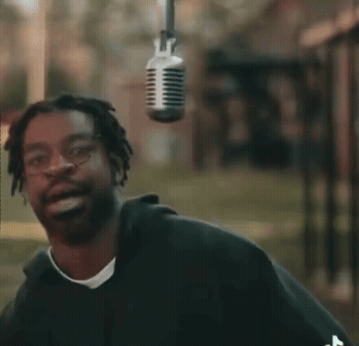 A Man Is Smiling In Front Of A Microphone Hanging From The Ceiling GIF