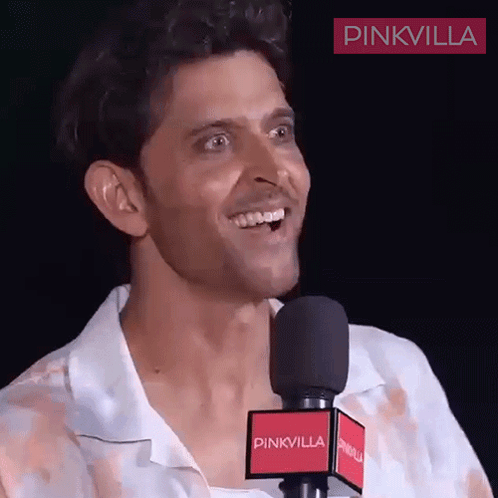 A Man Is Smiling In Front Of A Microphone That Says Pinkvilla On It GIF