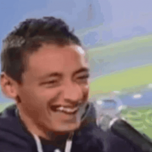 A Man Is Smiling In Front Of A Microphone While Sitting In Front Of A Field . GIF