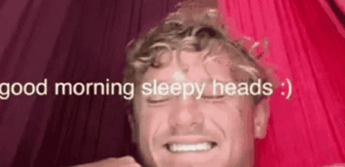 A Man Is Smiling In Front Of A Pink Curtain With The Words `` Good Morning Sleepy Heads '' Written On It . GIF
