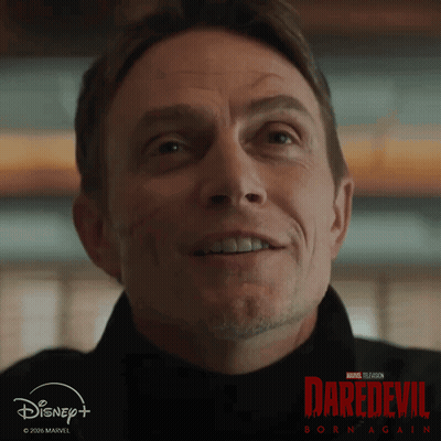 A Man Is Smiling In Front Of A Poster For Daredevil GIF
