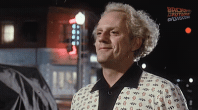 A Man Is Smiling In Front Of A Sign That Says Back To The Future On It GIF
