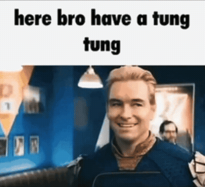 A Man Is Smiling In Front Of A Sign That Says Here Bro Have A Tung Tung . GIF