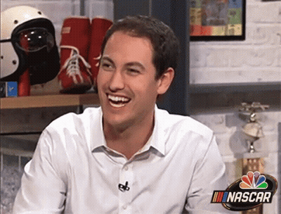 A Man Is Smiling In Front Of A Sign That Says Nascar GIF