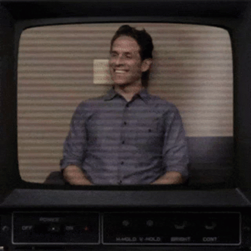 A Man Is Smiling In Front Of A Tv Screen That Says Hold V Hold GIF