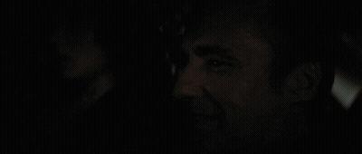 A Man Is Smiling In The Dark With A Woman In The Background GIF